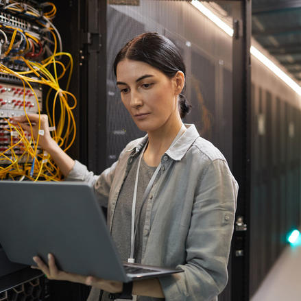 Technician checking a network with her laptop in the server room.